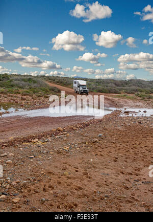 La trazione a quattro ruote motrici CAMPER / MOTORHOME circa a guidare attraverso acqua a creek incrocio su Australian Outback road orlate da una bassa vegetazione dopo la pioggia Foto Stock