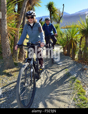 Ciclisti uomo e donna su bici elettriche, e-bike, sulle rive del lago Wanaka, Frankton, Queenstown, South Island, Nuova Zelanda Foto Stock