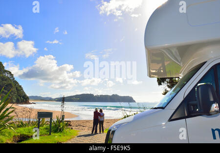 Un uomo e una donna di fronte al loro Maui noleggio camper guardando la vista a Hot Water Beach sulla penisola di Coromandel, Isola del Nord, Nuova Zelanda Foto Stock