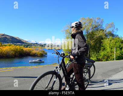 Signora ciclista su una bicicletta elettrica E-Bike, guardando il panorama sulle rive del Lago Wanaka, Frankton, Nr Queenstown, Isola del Sud, Nuova Zelanda Foto Stock