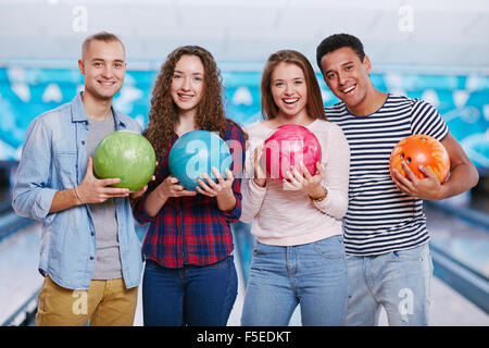 Allegro amici con le palle da bowling guardando la fotocamera Foto Stock