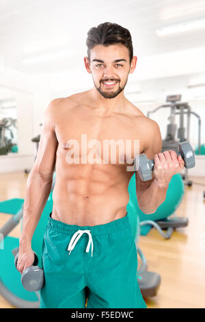 Bello e montare il giovane uomo che esercitano con manubri in palestra Foto Stock