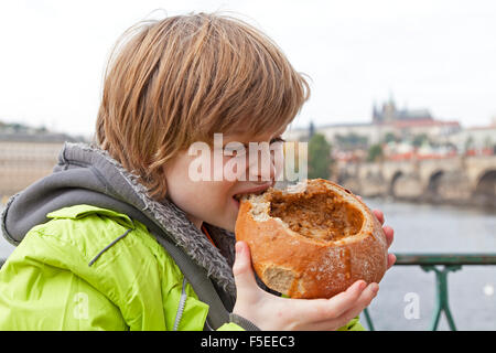 Ragazzo di mangiare zuppa di gulasch in pane nella parte anteriore del castello e il Ponte Carlo a Praga Repubblica Ceca Foto Stock