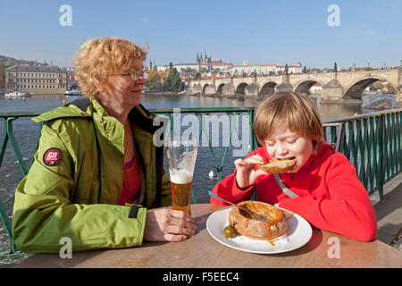 Ragazzo di mangiare zuppa di gulasch in pane nella parte anteriore del castello e il Ponte Carlo a Praga Repubblica Ceca Foto Stock