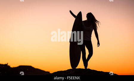 Silhouette di donna che trasportano le tavole da surf, Malibu, California, Stati Uniti d'America Foto Stock