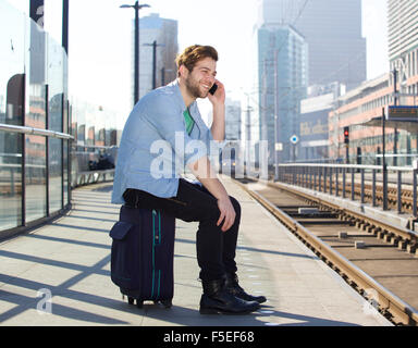 Ritratto di un uomo felice parlando al telefono cellulare in attesa del treno Foto Stock