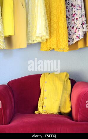 Abiti di colore giallo e giallo cardigan su un velluto rosso sedia Foto Stock