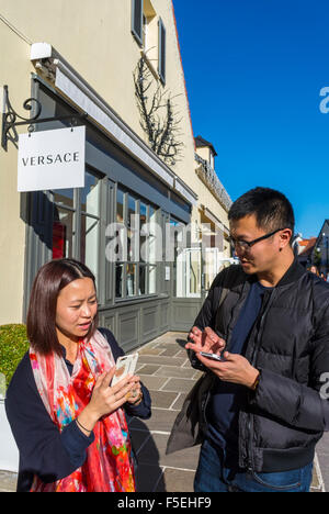 Parigi, Francia, Cinese giovane Shopping i negozi di lusso in 'La Vallee Village', sconto per negozi, Asian utilizzando gli smart phone, iphone su strada Foto Stock