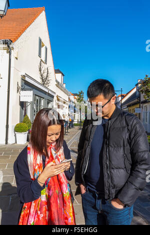 Parigi, Francia, Cinese giovane Negozi in 'La Vallee Village', sconto per negozi, Asian utilizzando gli smart phone, iphone su strada Foto Stock