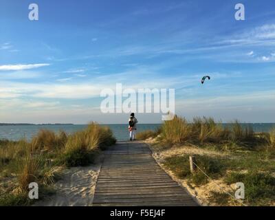 Vista posteriore di una donna in piedi sulla spiaggia guardando kiteboarder, La Rochelle, Francia Foto Stock