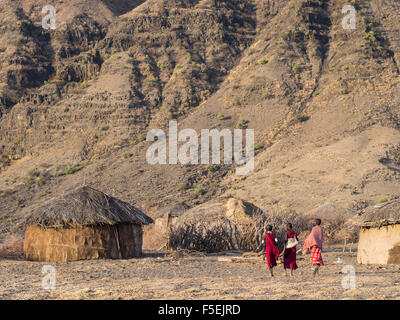 Tre bambini a camminare in un villaggio Masai di fronte all'Ol Doinyo Lengai nella Regione di Arusha, Tanzania Africa a sunrise. Foto Stock