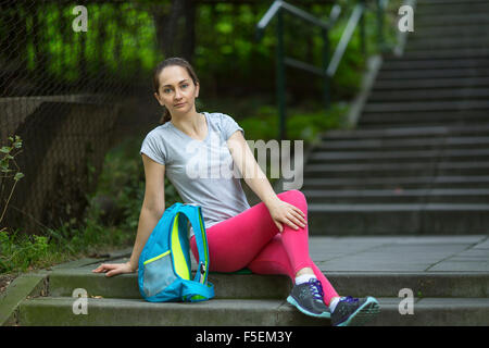 Atleta giovane ragazza seduta sulle scale di pietra nel parco. Foto Stock