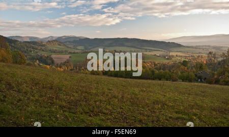 Serata autunnale nel Beskids montagne vicino villaggio Nydek con prato e colorati di alberi, le gamme della montagna e cielo blu con nuvole Foto Stock