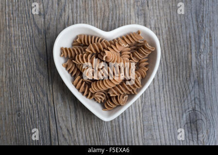 Cereali integrali, farro fusilli in un cuore piatto sagomato Foto Stock