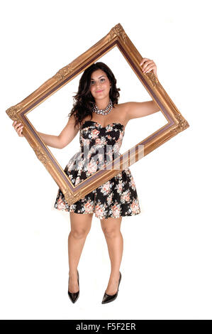 Una bellissima giovane adolescente in un bel vestito con in mano una golden vecchia cornice immagine, stando in studio in tacchi alti per il bianco Foto Stock