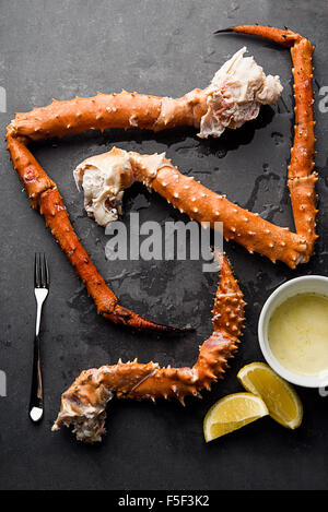 Re crab gambe disposte su un sfondo di ardesia con burro, limoni e una forcella di frutti di mare Foto Stock