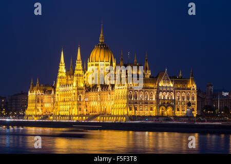 Una vista laterale del parlamento ungherese edificio lungo il fiume Danubio a notte con l'edificio illuminato e riflessi nel Foto Stock