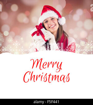 Immagine composita della donna attraente indossando santa hat con dono Foto Stock