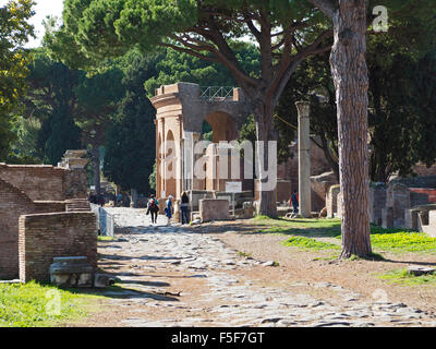 I turisti camminando sulla Osta Antica Via Decumana road, con l'ingresso al teatro visibile in background. Italia Foto Stock