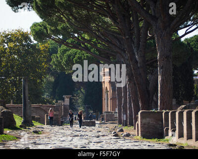 I turisti camminando sulla Osta Antica Via Decumana road, con l'ingresso al teatro visibile in background. Italia Foto Stock