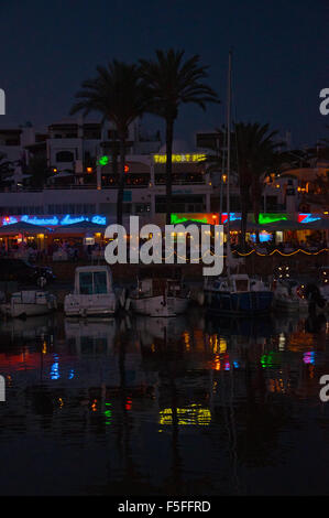 Bella marina con piccole imbarcazioni e colorate insegne al neon riflesso in acqua al tramonto Foto Stock