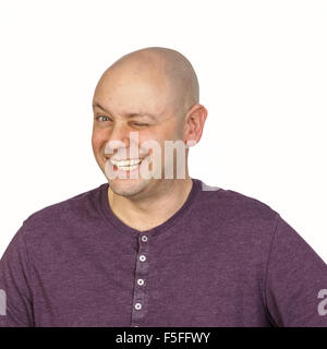 Big wink da un uomo calvo in studio su sfondo bianco. Egli indossa una viola abbottonata t-shirt con un giro collo. Foto Stock