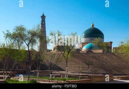 Uzbekistan, Khiva, un giardino in centro città con l'Islam Kodija minareto e Mahmud mausoleo in background Foto Stock