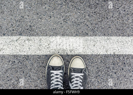 Uomo in piedi alla linea di confine sulla pavimentazione urbana, vista dall'alto del giovane maschio piedi indossando scarpe da ginnastica, in attesa dietro la linea Foto Stock