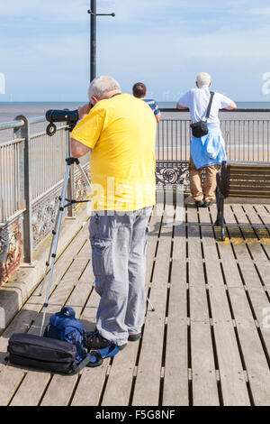 Uomo che guarda attraverso un telescopio o ambito vista sul mare o sulla spiaggia dalla fine del molo a Skegness, Lincolnshire, England, Regno Unito Foto Stock