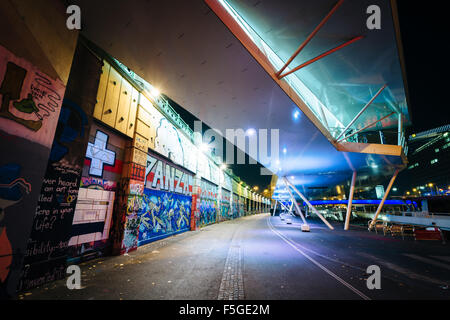 Graffiti su un muro e moderno edificio lungo il canale del Danubio di notte, a Vienna, Austria. Foto Stock