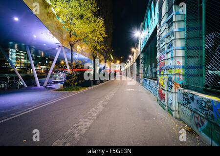 Graffiti su un muro e moderno edificio lungo il canale del Danubio di notte, a Vienna, Austria. Foto Stock