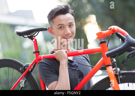 Giovane uomo che porta bicicletta sulla spalla Foto Stock