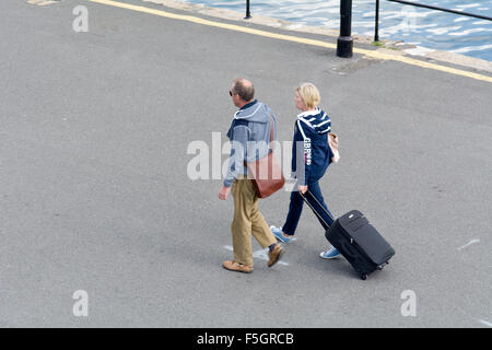 L uomo e la donna tirando la valigia su ruote a piedi attraverso Sutton Harbour, Plymouth Devon, Inghilterra Foto Stock