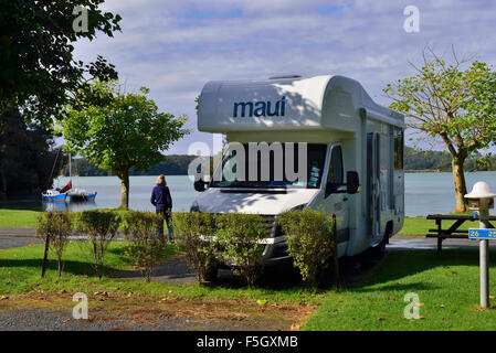 Femmina in tour in motoscafo guarda verso la baia dal campeggio bordo acqua in Paihia, Baia delle Isole, Isola del Nord, Nuova Zelanda Foto Stock