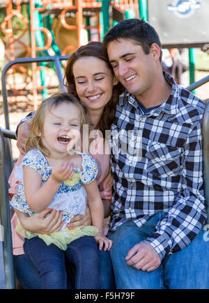 Padre, Madre e carino giovane figlia sul park merry-go-round Foto Stock