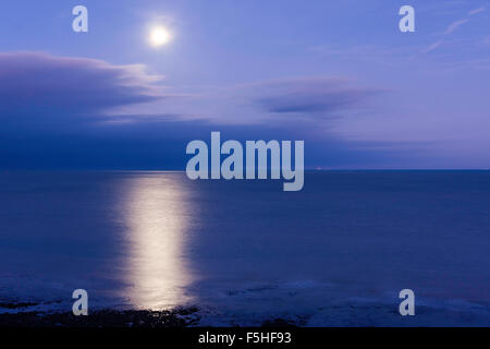 Super luna splendenti in un viola chiaro cielo blu sopra un mare di vongole, il canale della Manica, off alla costa del Kent a Ramsgate, con grande riflessione. Alcune nuvole. Foto Stock