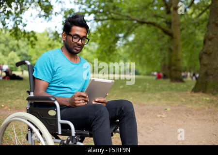 Giovani indiani uomo in sedia a rotelle usando un computer tablet Foto Stock