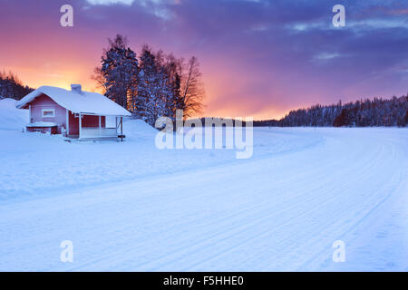 Un piccolo cottage sul bordo di un lago ghiacciato. Fotografato vicino a Levi in Lapponia finlandese a sunrise. Foto Stock