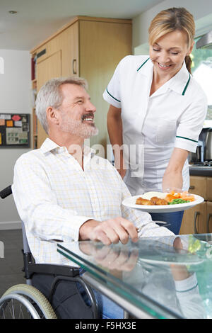 Accompagnatore che serve pasti a uomo in carrozzella a casa Foto Stock