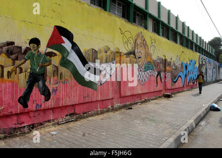 Rafah nella striscia di Gaza, Territori palestinesi. 5 Novembre, 2015. Un ragazzo palestinese cammina davanti a un graffiti raffiguranti un palestinese sventolando la sua bandiera nazionale a sostegno della terza sollevazione palestinese, a Rafah nel sud della striscia di Gaza il 5 novembre 2015. L'attuale ondata di violenza è scoppiata a metà settembre, alimentato dalle voci che Israele stava cercando di aumentare la presenza ebraica a Gerusalemme e poi a diffondersi rapidamente in tutta Israele e la Cisgiordania e la striscia di Gaza Credito: Abed Rahim Khatib/immagini APA/ZUMA filo/Alamy Live News Foto Stock