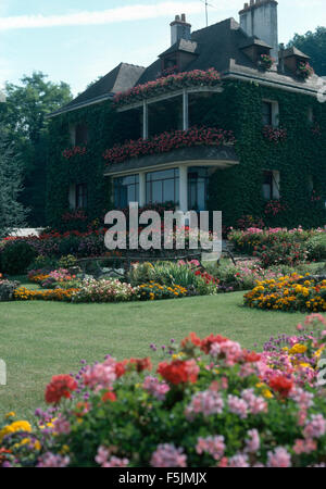 Luminose annuari crescente in bordi accanto a prato nel giardino della grande casa francese con colorate scatole di finestra Foto Stock