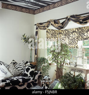 Nero+bianco stampa animale divano e cuscini in novanta soggiorno con tessuto drappeggiato in pole nella finestra di cui sopra Foto Stock