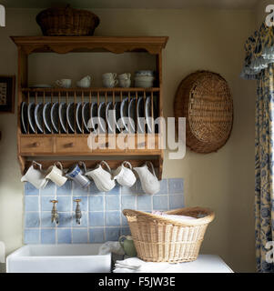 Piastra di pino di rack e di fila di brocche sopra il lavabo in cottage cucina con un cesto della biancheria sul piano di lavoro Foto Stock