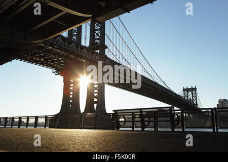 Il sole sorge tra i supporti di acciaio del ponte di Manhattan a New York City Foto Stock