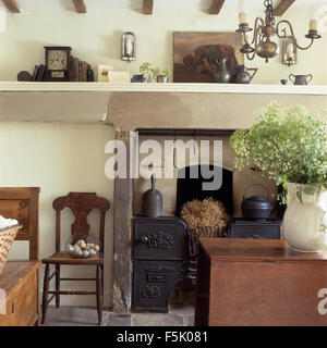 Antiquariato sedia di legno accanto al camino con un originale in ghisa forno gamma nel caminetto in un cottage sala da pranzo Foto Stock