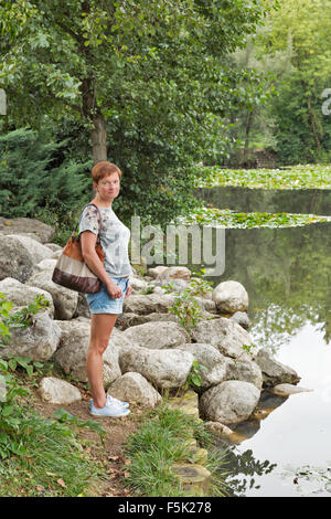 Persone di mezza età abbronzata donna caucasica si erge sulle rive del pittoresco lago di Foto Stock