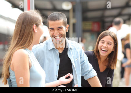 Tre amici a parlare e ridere tenendo una conversazione in una stazione ferroviaria Foto Stock