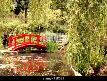 Rosso stile cinese ponte sopra un ruscello con gli alberi di salice sulla banca in un paese grande giardino Foto Stock
