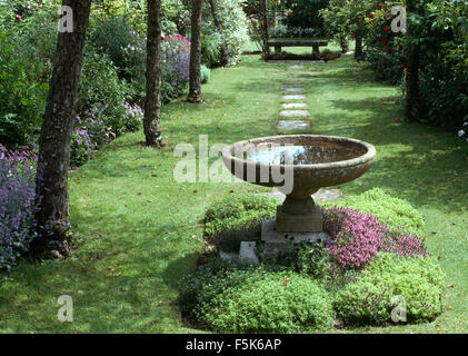 Pietra Antico Bagno uccelli sotto-piantate con bassa la coltivazione di piante in un piccolo viale con pavimentazione attraverso erba falciata Foto Stock