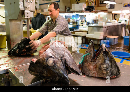 Un uomo taglio di grandi teste di tonno al mercato del pesce Tsukiji a Tokyo in Giappone Foto Stock